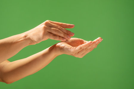 Close up of hands creating a gesture against a bright green backdrop, emphasizing skin tone and elegance. Beauty concept, skin care, and cream product presentation.の写真素材