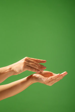 Close up of hands creating a gesture against a bright green backdrop, emphasizing skin tone and elegance. Beauty concept, skin care, and cream product presentation.の写真素材