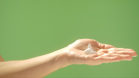 A hand holding a dollop of white cream contrasted against a clean green background, showcasing skincare. Beauty concept, skin care, and cream product presentation.の写真素材