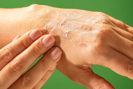Close up of a hand applying moisturizing cream on the skin against a vibrant green background. Beauty concept, skin care, and cream product presentation.の写真素材