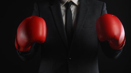 A businessman wearing a dark suit and red boxing gloves, symbolizing strength and competition.の写真素材