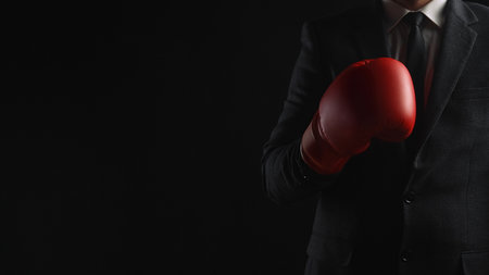 A businessman dressed in a suit and tie wears a red boxing glove, symbolizing competition and determination.の写真素材