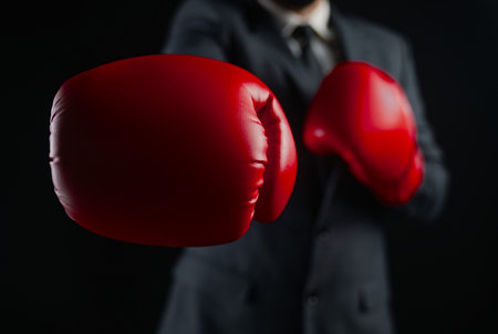 A close up of a businessman wearing a suit and red boxing gloves, symbolizing competition and readiness.の写真素材