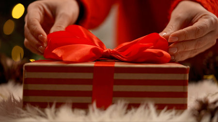 Close up of hands tying a red ribbon on a striped gift box, capturing the essence of gift giving.の写真素材