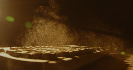 A warm light illuminates dust particles as they float above a computer keyboard, creating an...