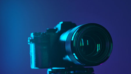 Close up of a professional digital camera mounted on a tripod, illuminated by blue light against a dark background.の写真素材