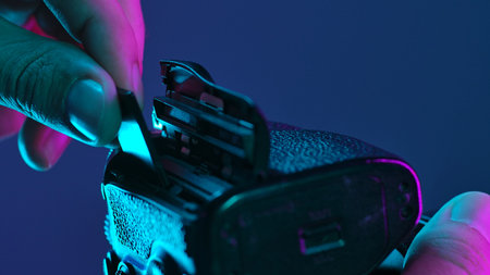 A hand inserting a memory card into a camera under vibrant purple and blue lighting, creating a futuristic ambiance.の写真素材