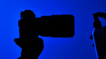 Silhouette of a hand spraying sprayer in front of a camera lens against a vibrant blue background. Concept of cleaning and caring for photographic equipment.の写真素材