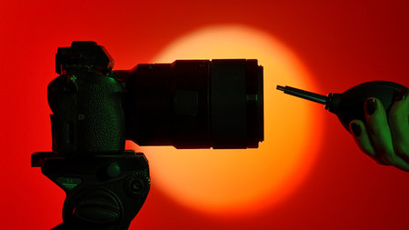 A silhouette of a camera lens and lens blower against a vivid red background with bright round light from a spotlight, emphasizing photography equipment.の写真素材