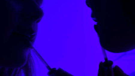 Close up of a woman reflected in a mirror and applying lip gloss in a dark room lit by blue neon lightの写真素材