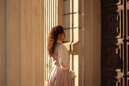 An elegant woman in a vintage dress stands by an old stone columnの写真素材