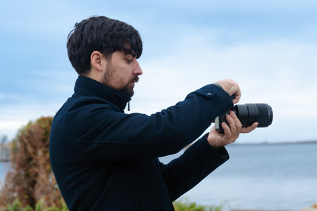 Man Adjusting Camera Settings by the Waterの写真素材