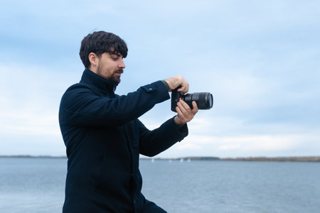 Man Adjusting Camera Settings by the Waterの写真素材