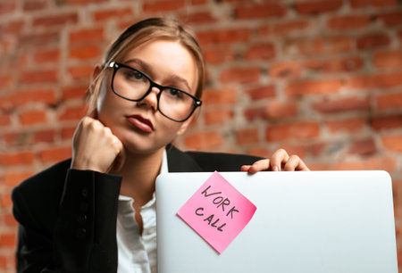 Young Woman in Glasses Holding Laptop with Noteの写真素材
