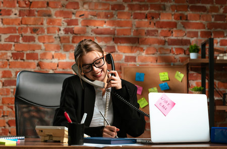 Businesswoman on Phone Taking Notes in Brick Wall Officeの写真素材