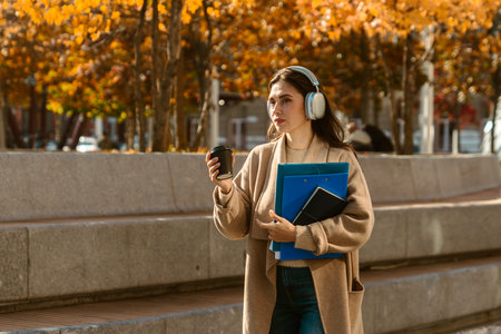 Woman Walking with Headphones and Coffee in Autumn Cityの写真素材