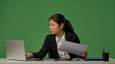 A young Korean businesswoman in a black suit looks through documents with graphsの写真素材