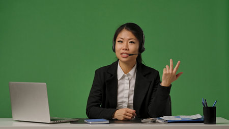 A young Korean businesswoman in a black suit and headset talks to the camera