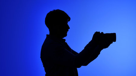 Backstage Silhouette of Photographer Holding Camera Against Blue Backgroundの写真素材