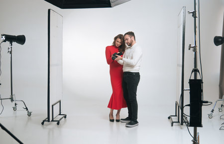 Photographer and model in a red dress reviewing camera images in a studio setting with lighting equipment.の写真素材