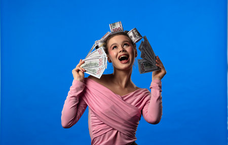 A woman in a pink blouse, with curlers in the shape of banknotes in her hair against a blue...