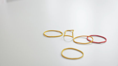 Scattered multicolored rubber bands on a clean white desk, close-up, illuminated workspace.の写真素材