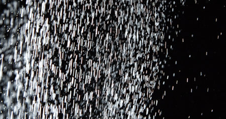 Dust particles or white snow scatter haphazardly through the air and shimmer in the spotlight, isolated on a black background. Background with overlay effect.の写真素材