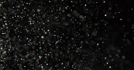 Dust particles or white snow scatter haphazardly through the air and shimmer in the spotlight, isolated on a black background. Background with overlay effect.の写真素材