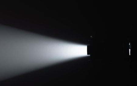 A powerful, focused beam of white light emanating from a spotlight in a dark room creates striking...