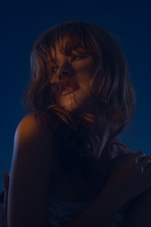 A captivating portrait of a young female model, illuminated by dramatic blue muted lighting that...