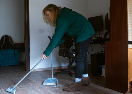 A young woman in casual clothing is sweeping the floor in a home office. The scene shows a clean and...