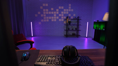 Daily lifestyle concept. Young adult man home, shot of male living room with neon light, desk with computers, keyboard and gaming chair, modern streamer podcaster blogger room setup.の写真素材