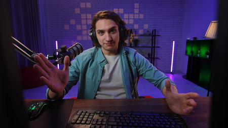 Daily lifestyle concept. Young adult man spending time at home, man streamer gamer sits at desk recording stream, talking online by video call on computer, looks at camera, person pov.の写真素材