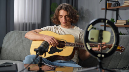 Daily lifestyle concept. Young adult man spending time at home, man sits on the couch with acoustic...