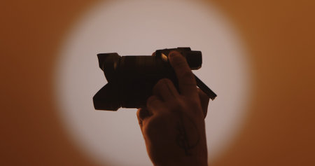 A silhouette of a hand holding a camera against a warm, softly lit backdrop, capturing the essence...