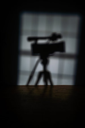 The shadow of a professional video camera on a tripod stands in a dark studio, suggesting filming or broadcast production. Backstage photo shoot.の写真素材