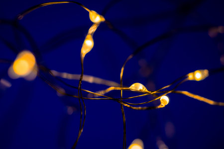 Close up of glowing string lights emitting a warm yellow hue on a deep blue backdrop, creating a...