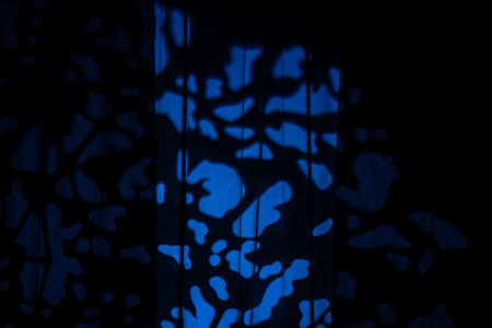 Blue light spots form an abstract bokeh pattern on dark curtains, creating a moody cinematic studio...