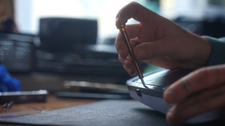 A detailed view of a person hand using a screwdriver to repair or assemble an electronic device.