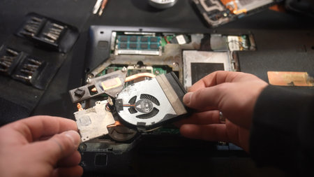 Close up view of hands disassembling a laptop, focusing on internal components and fan removal.