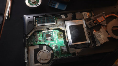 Close up of a disassembled laptop revealing the motherboard and internal components under repair.