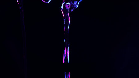 Abstract close up of glowing blue and purple water streams falling against a deep black background, illuminated with dramatic neon light and leaving empty copy space in the center for text or design.の写真素材