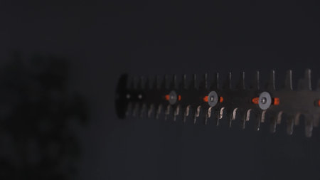 Focused view on the metal teeth of a hedge trimmer blade with a dark blurred background.