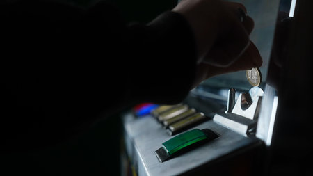 Atmospheric close up of a player hand inserting a coin into the slot of an old gambling machine.