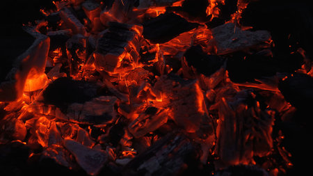 Close up of glowing charcoal embers with orange heat and flying sparks in a dark grill. Dramatic...