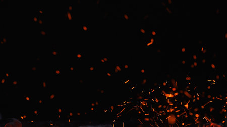 Floating orange sparks and embers rising in the dark, creating an abstract fire texture with copy...