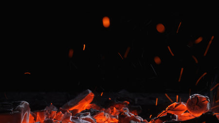 Close up of glowing charcoal embers with orange heat and flying sparks in a dark grill. Dramatic...