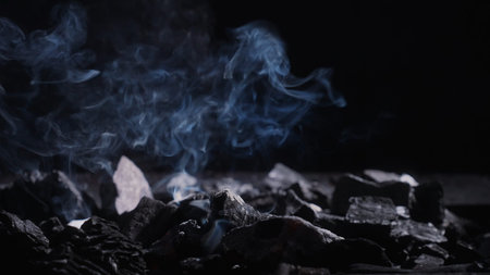 Swirling smoke above black charcoal in a grill, creating a moody background for barbecue, heat, smoldering fuel, fire safety, and air pollution concepts.の写真素材