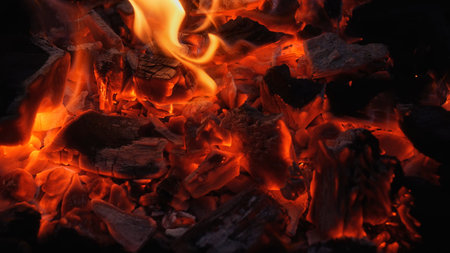 Close up of glowing charcoal embers with orange heat and flying sparks in a dark grill. Dramatic...