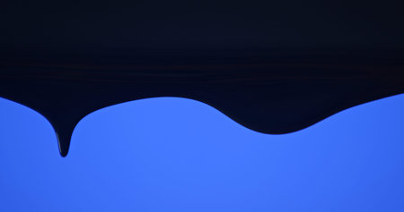 Close up of black paint flowing down a pane of glass against a soft blue background, creating a minimalist abstract texture for design and advertising uses.の写真素材